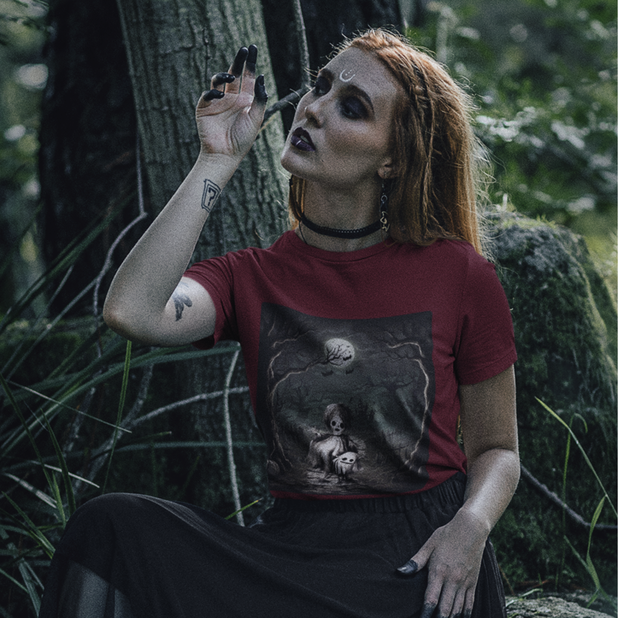 Person wearing a cardinal t-shirt with a graphic design, sitting in a forest setting.