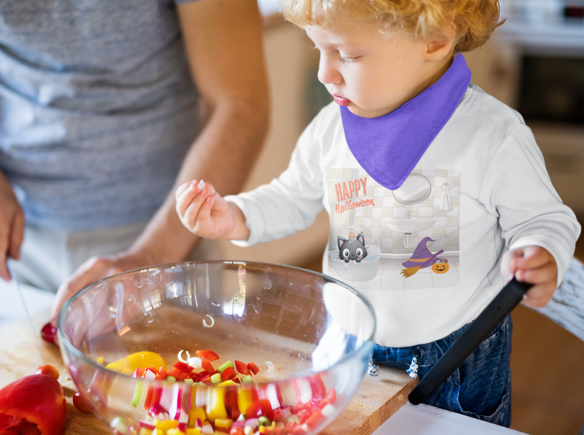 Child wearing a Halloween-themed shirt and bib, standing at a table with a bowl of colorful candy.
