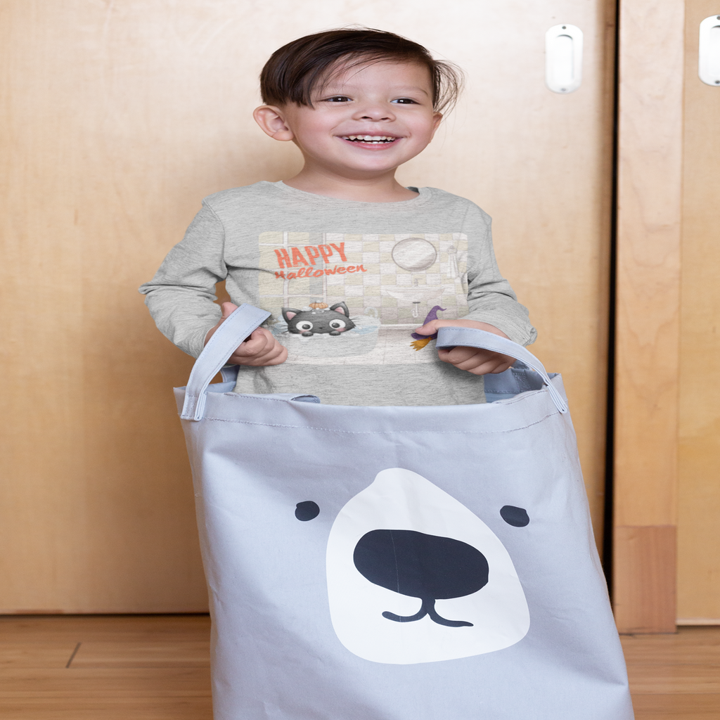 Child standing inside a gray laundry basket with a bear design, wearing a Halloween-themed shirt.