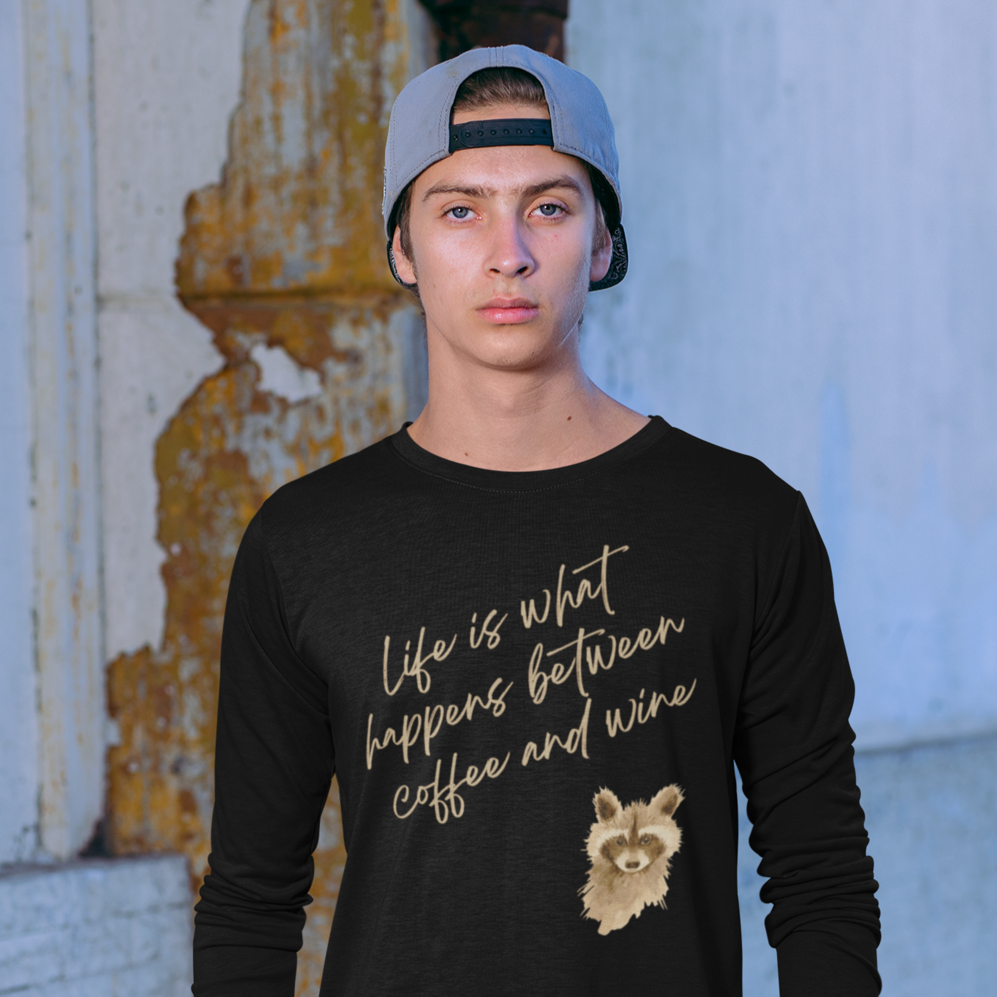 Person wearing a black long-sleeve shirt with text and a raccoon graphic, standing against a textured wall.
