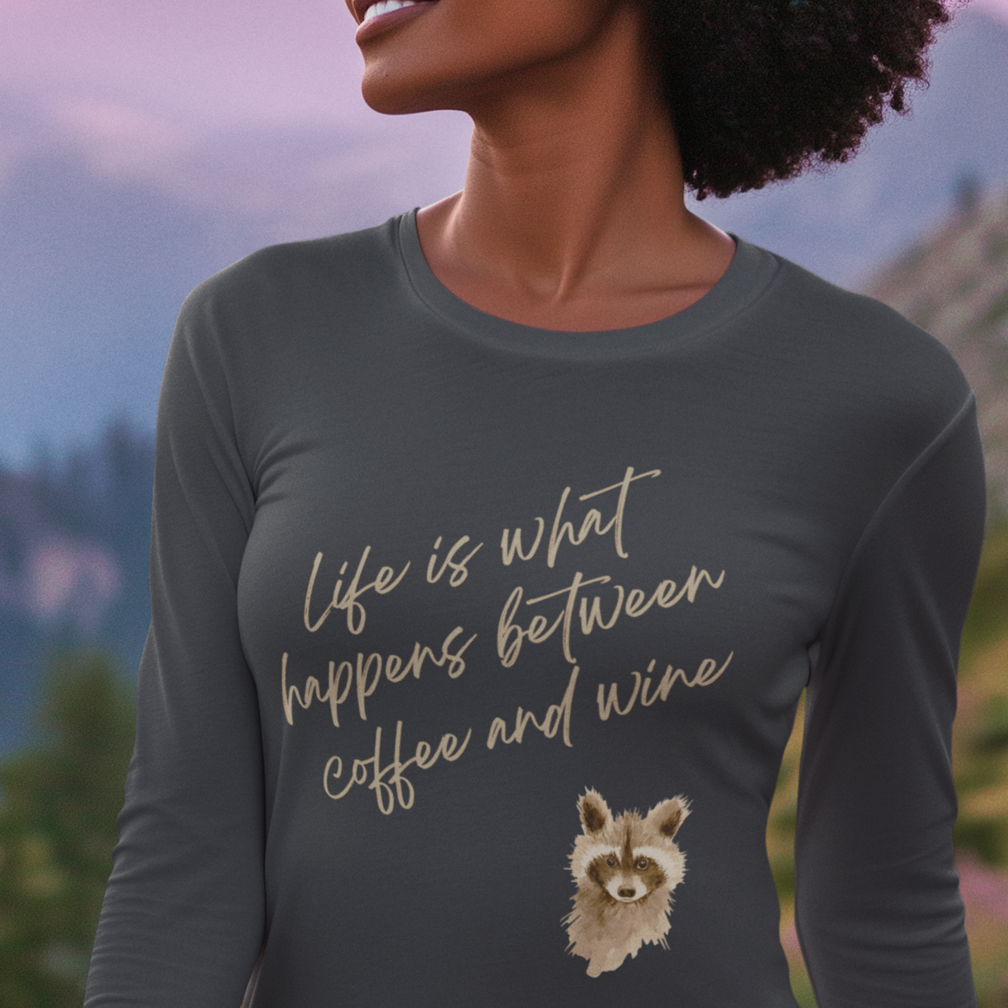 Person wearing a dark gray long-sleeve shirt with a raccoon illustration and text in a scenic outdoor setting.