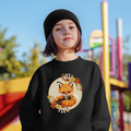 Child wearing a black sweatshirt with a fox and pumpkin design in an outdoor setting.