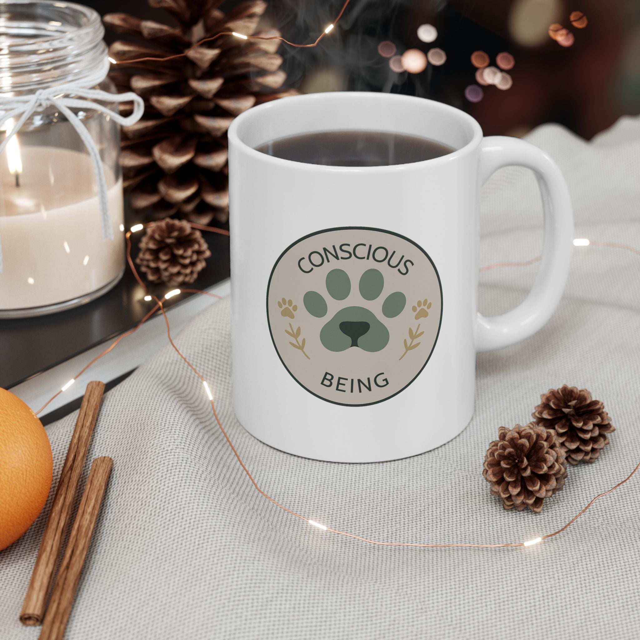 11 oz white ceramic mug with Conscious Being paw logo in soft green and neutral tones.