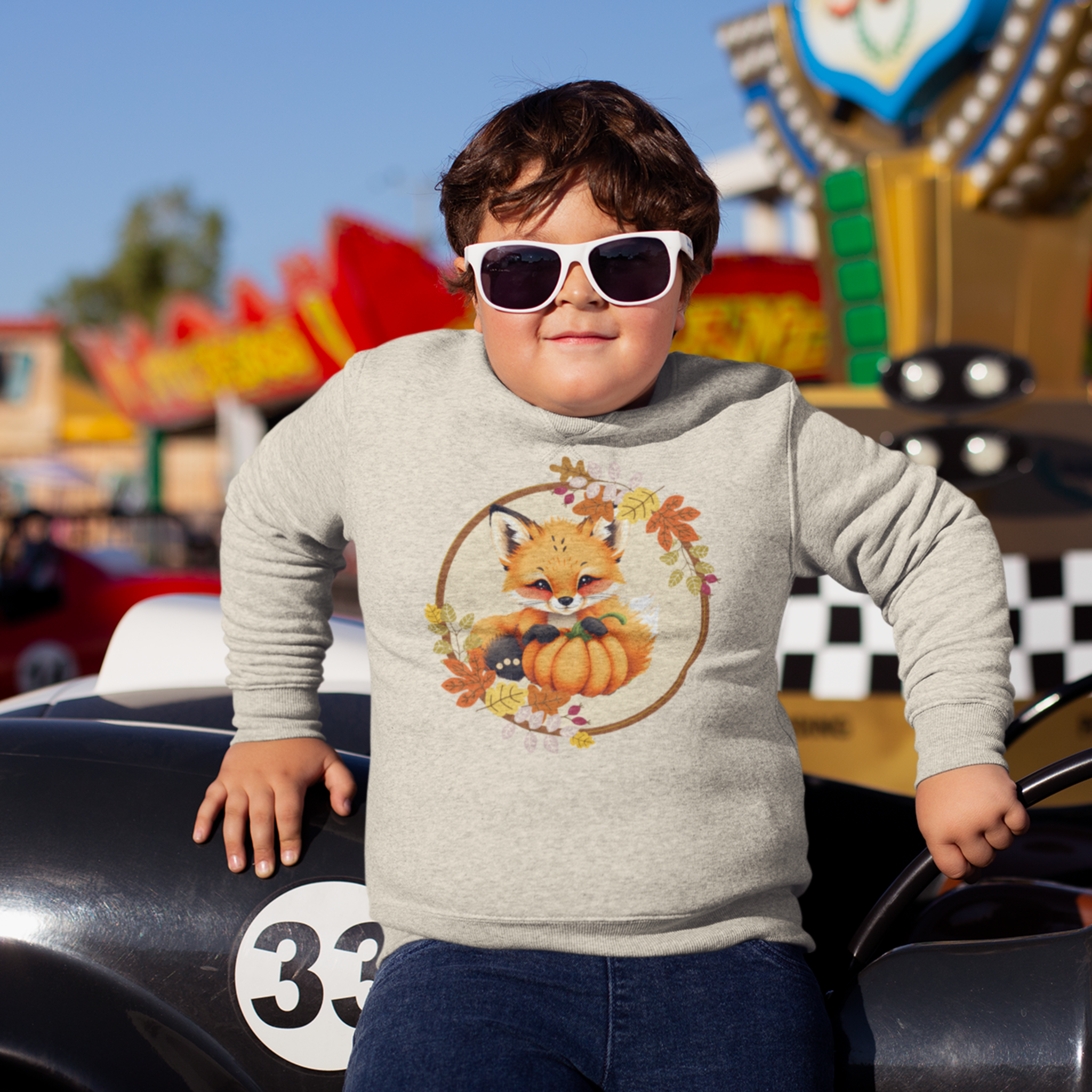 Child wearing sunglasses and a sweatshirt with a fox design at an amusement park.